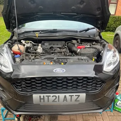 A black Ford Fiesta with the bonnet up on a driveway, ready for a service